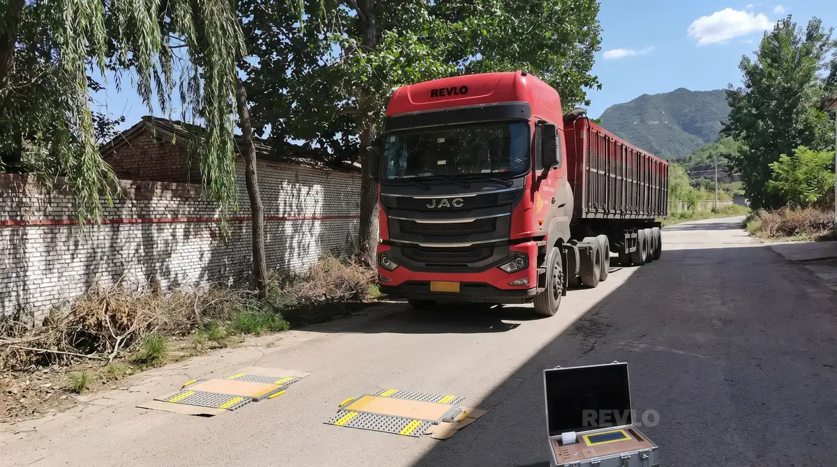 Caminhão com carreta basculante parado sobre as plataformas da balança, com a maleta do display aberta no chão
