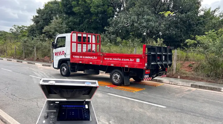 Caminhão parado sobre as plataformas da balança no acostamento de uma estrada, com a maleta do display aberta em primeiro plano